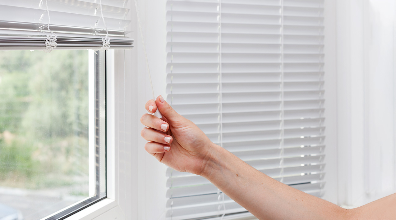 Hand pulling the blinds down on a window.